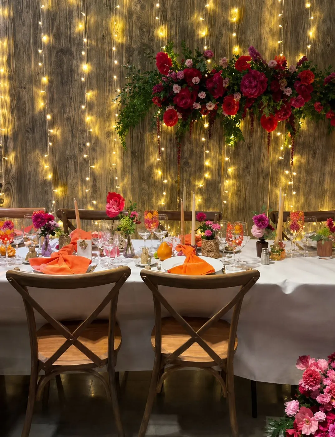 Image d'inspiration : table d'honneur, guirlandes lumineuses sur bois brut, roses rouges et serviettes orange